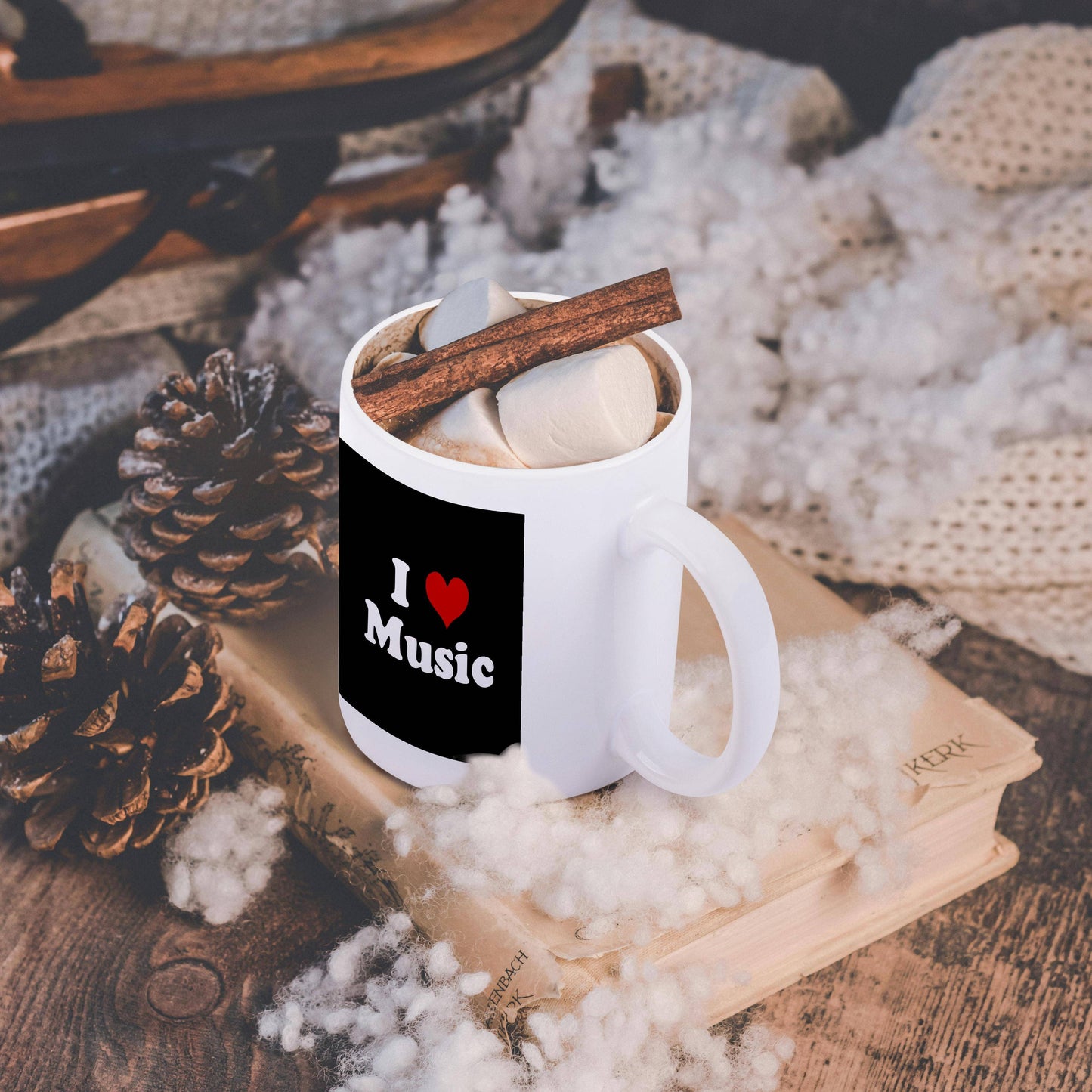 White mug with 'I ❤️ Music' text, cinnamon stick, and marshmallow on a textured surface.