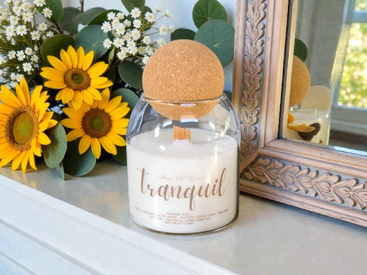 Candle labeled 'tranquil' on a surface with sunflowers and decorative mirror in the background