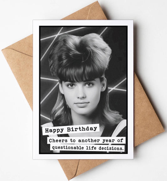 Birthday card with a photo of a person and humorous text, placed on a white surface with a brown envelope.