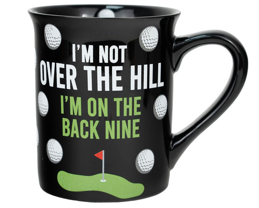 Black mug with golf-themed design and text 'I'm not over the hill, I'm on the back nine' on a white background.