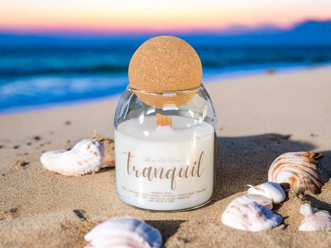 Candle labeled 'Tranquil' on a sandy beach with shells and ocean view